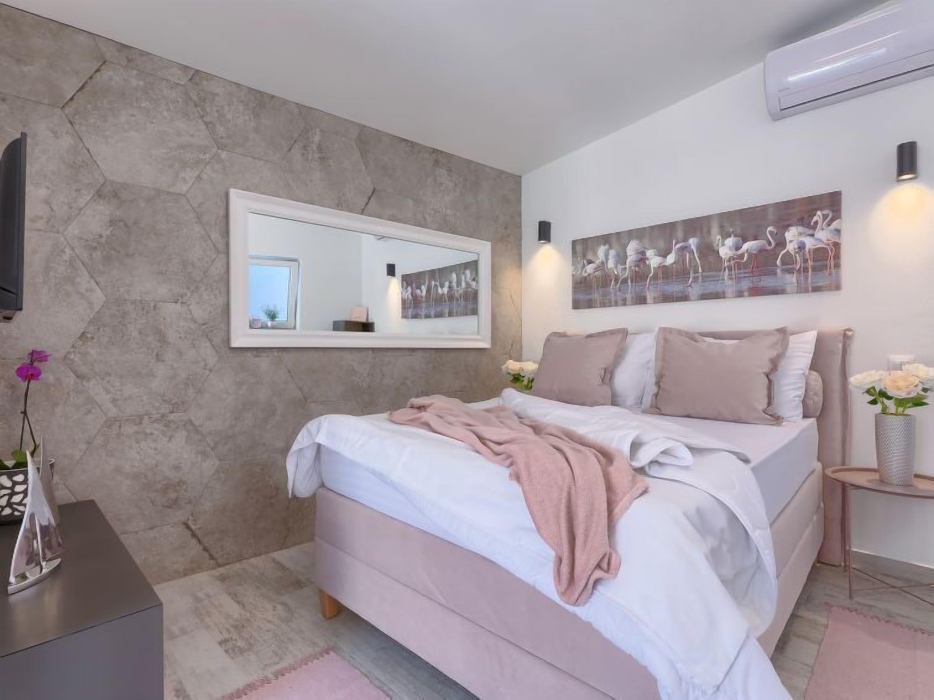 Une chambre à coucher avec un lit, un miroir, un tableau et un vase de fleurs.