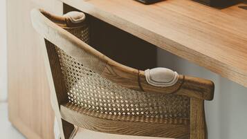 A wooden desk with a laptop, a coffee maker, and a tissue box. A wicker chair is positioned in front of the desk.