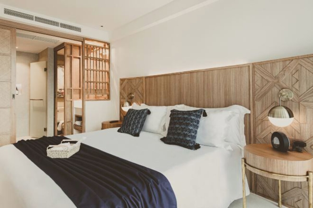 A hotel room with a bed, bedside table, lamp, and a wooden headboard.