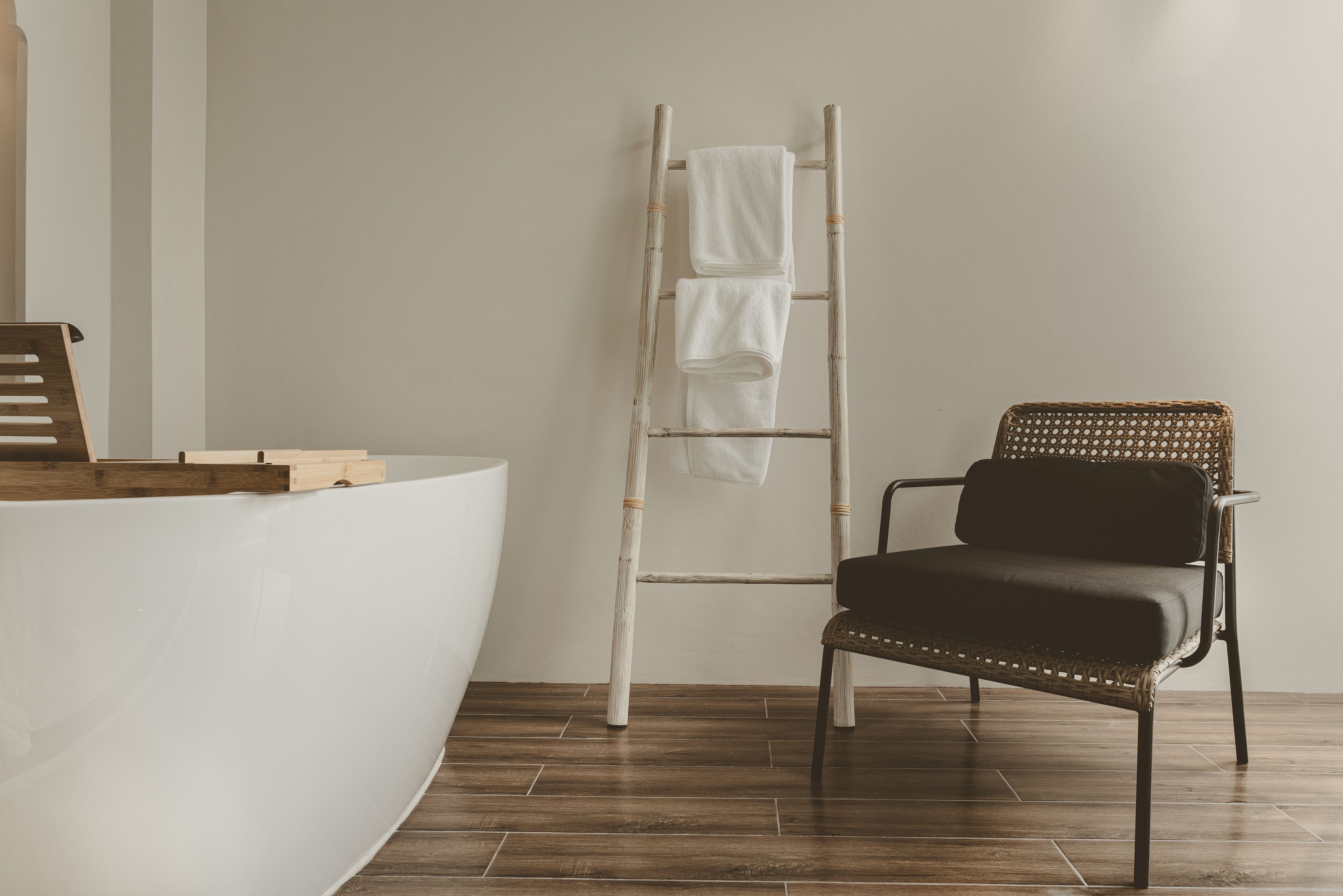 A bathroom with a wooden ladder, a black chair, and a white bathtub.