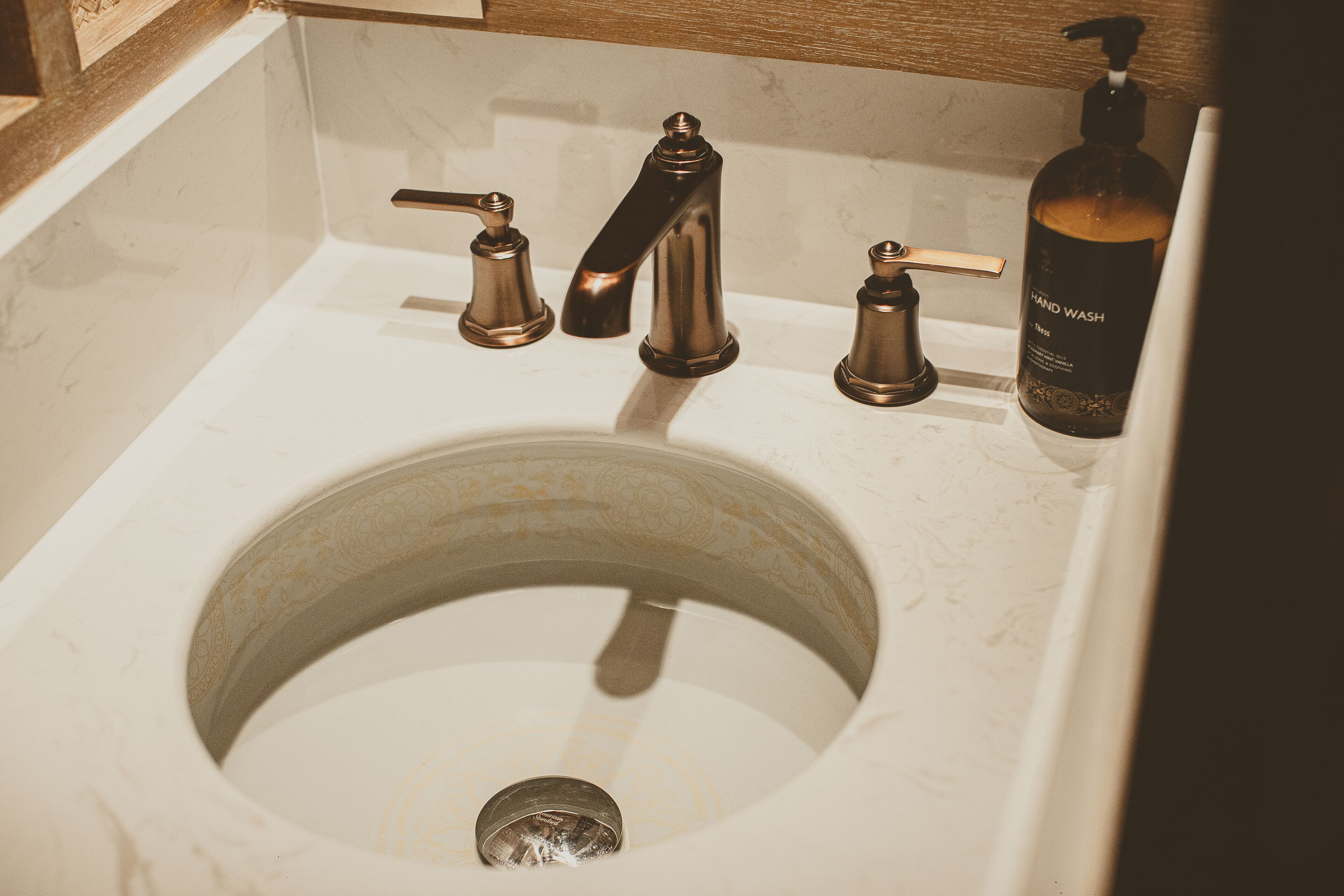 A bathroom sink with a single faucet, a soap dispenser, and a toilet.