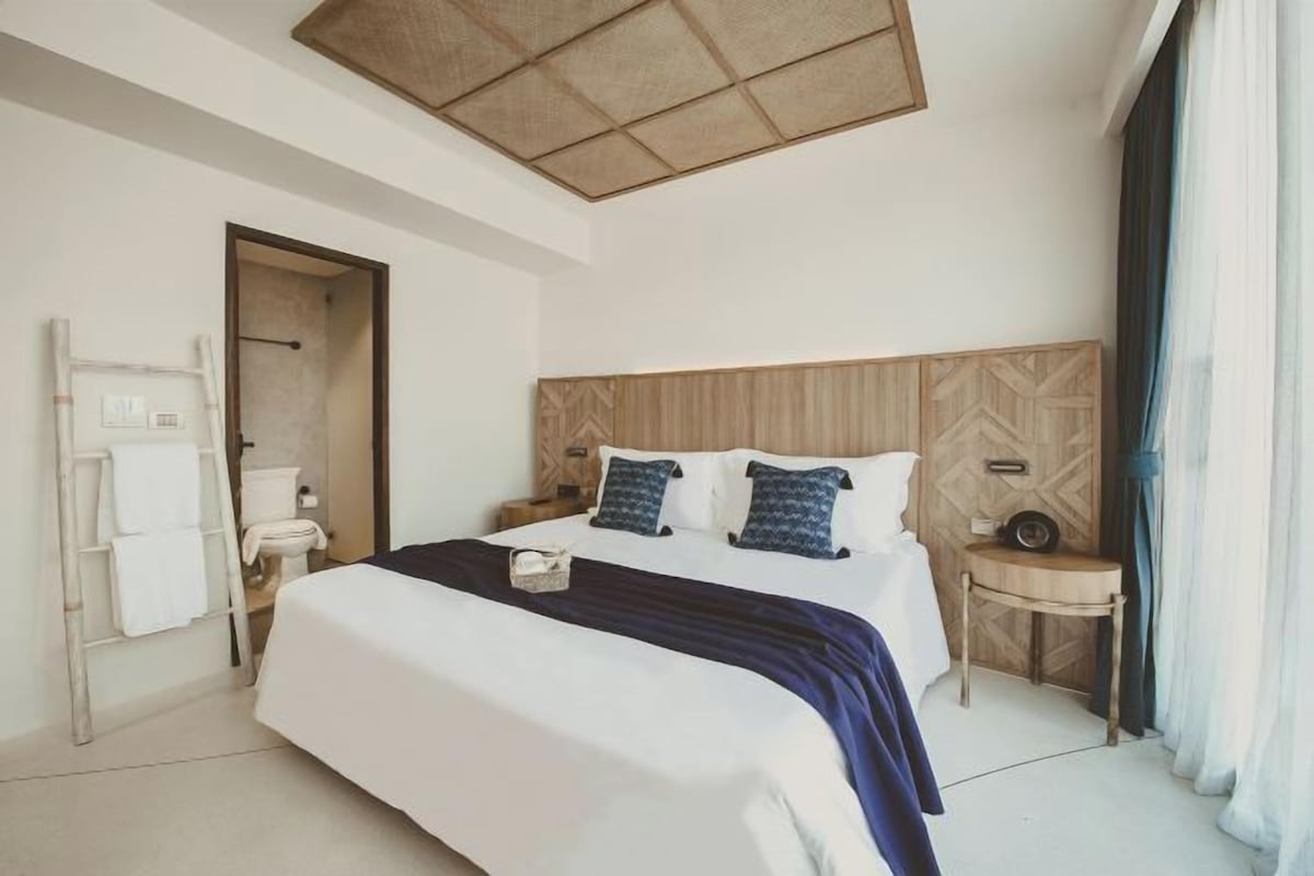 A hotel room with a large bed, a wooden headboard, a bedside table, and a window with curtains.