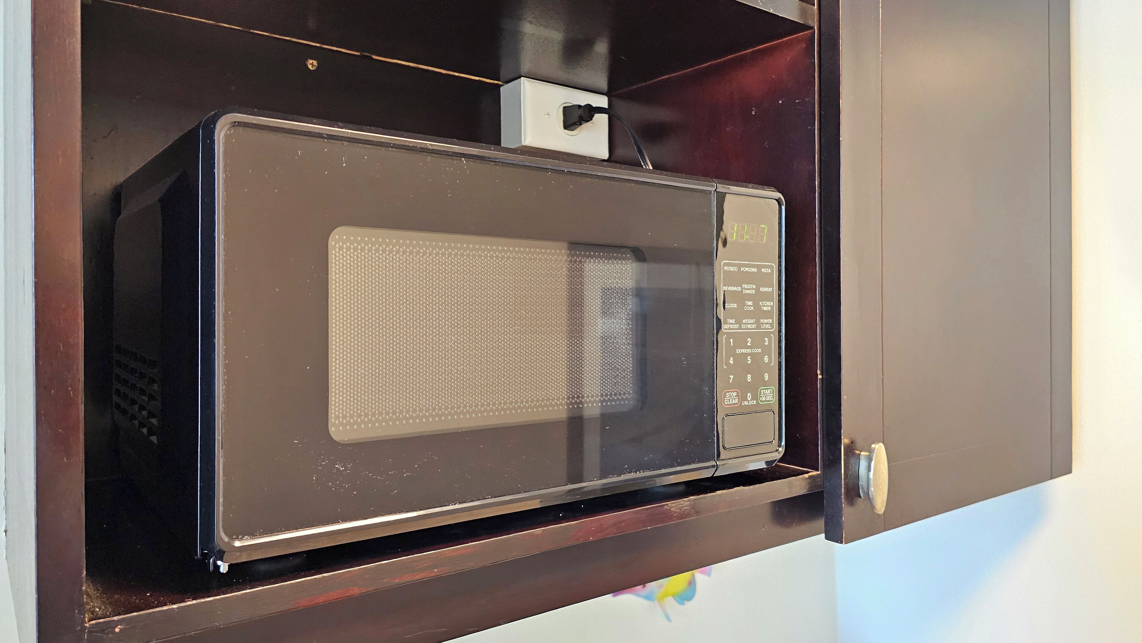 A microwave oven with a digital display, control panel, and a power cord plugged in.