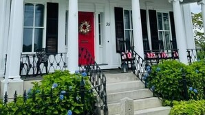 Un edificio de estilo colonial blanco con puerta roja, columnas y un balcón adornado con motivos rojos y blancos.