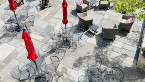 Un patio con suelo de piedra, sillas de metal y sombrillas rojas.
