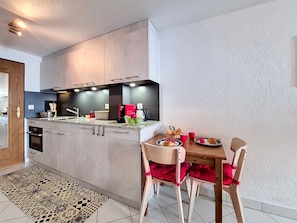 A modern kitchen with built-in appliances, a dining area with a table and chairs, and a patterned rug.
