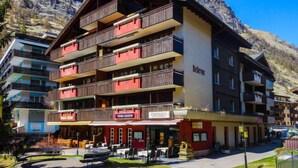 Un hotel a più piani con balconi, un ristorante e vista sulle montagne.