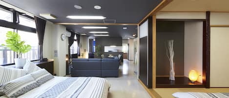A modern hotel room with a large bed, a sofa, a dining area, and a view of the city.
