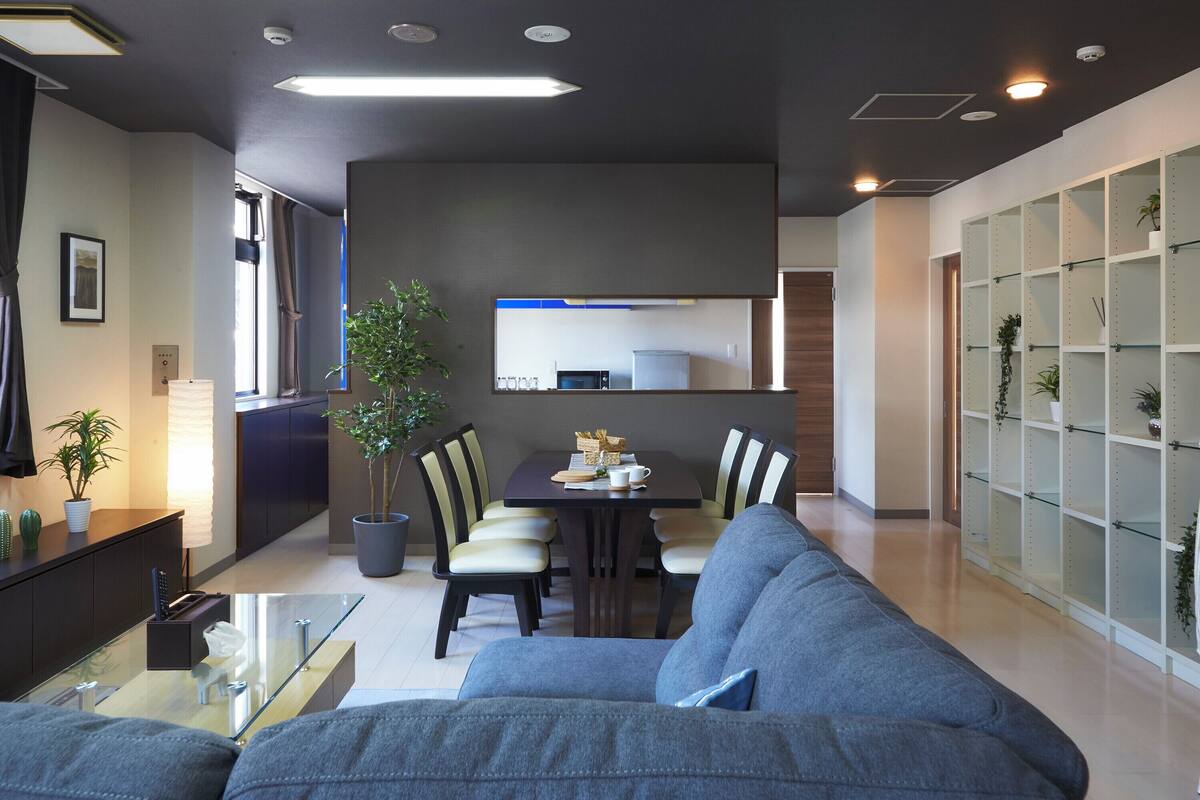 Una sala de estar moderna con un sofá gris, una mesa de comedor, sillas y una planta en maceta.