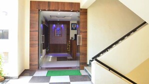 A modern hotel lobby with a glass entrance, a green mat, and a checkered floor. - The New Holiday Inn (Mahesana)