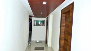 A hallway with white walls, a wooden door on the right, and a framed picture on the wall. - The New Holiday Inn (Mahesana)