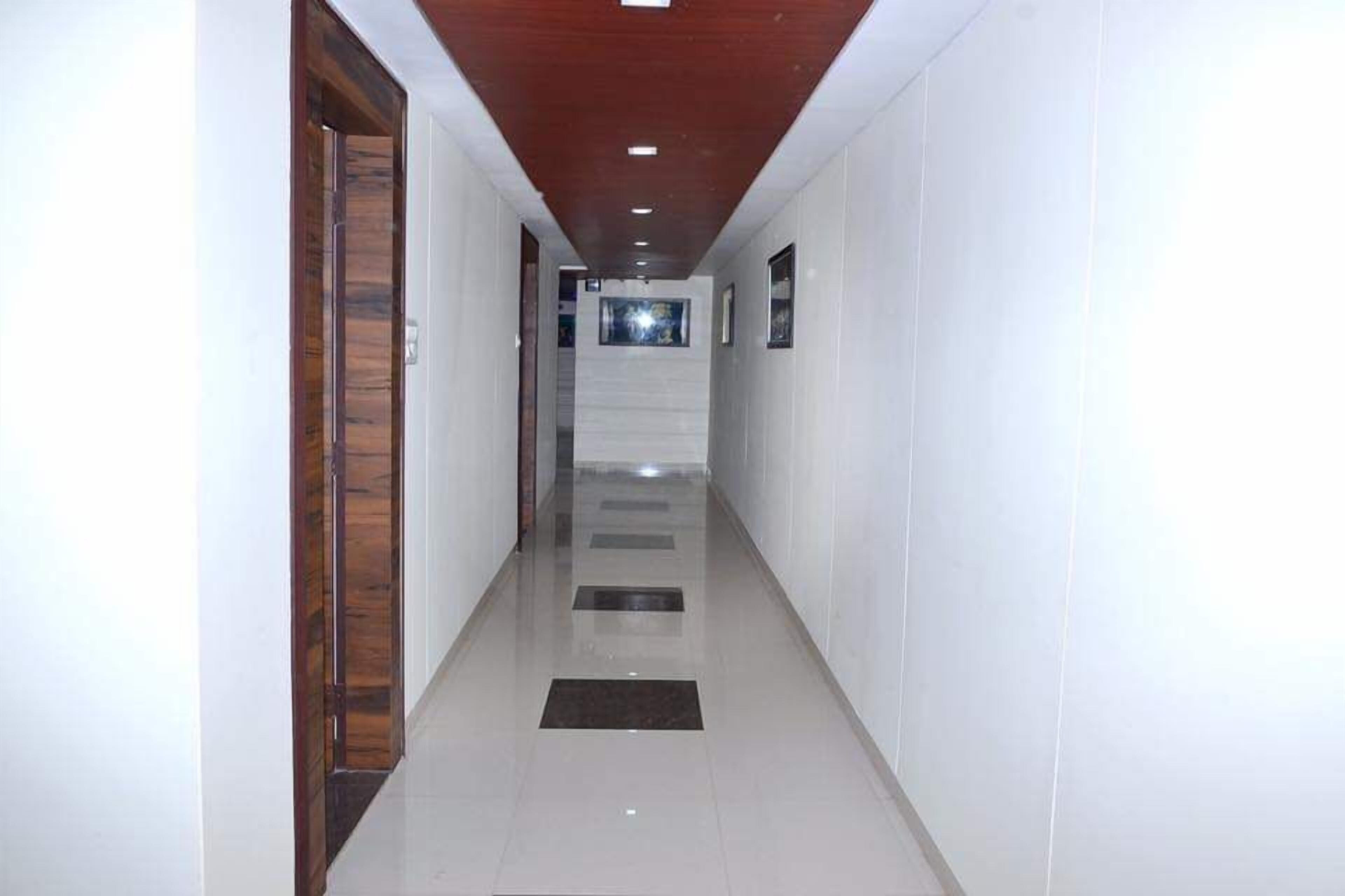 A hallway with white walls, a wooden door on the left, and recessed lighting on the ceiling.