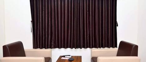 A room with a wooden table, two chairs, a small coffee table, and a large window with dark curtains.