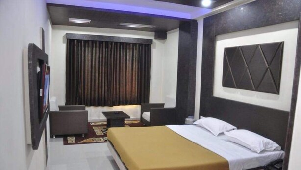 A hotel room with a bed, bedside table, and a desk with a chair. - The New Holiday Inn (Mahesana)