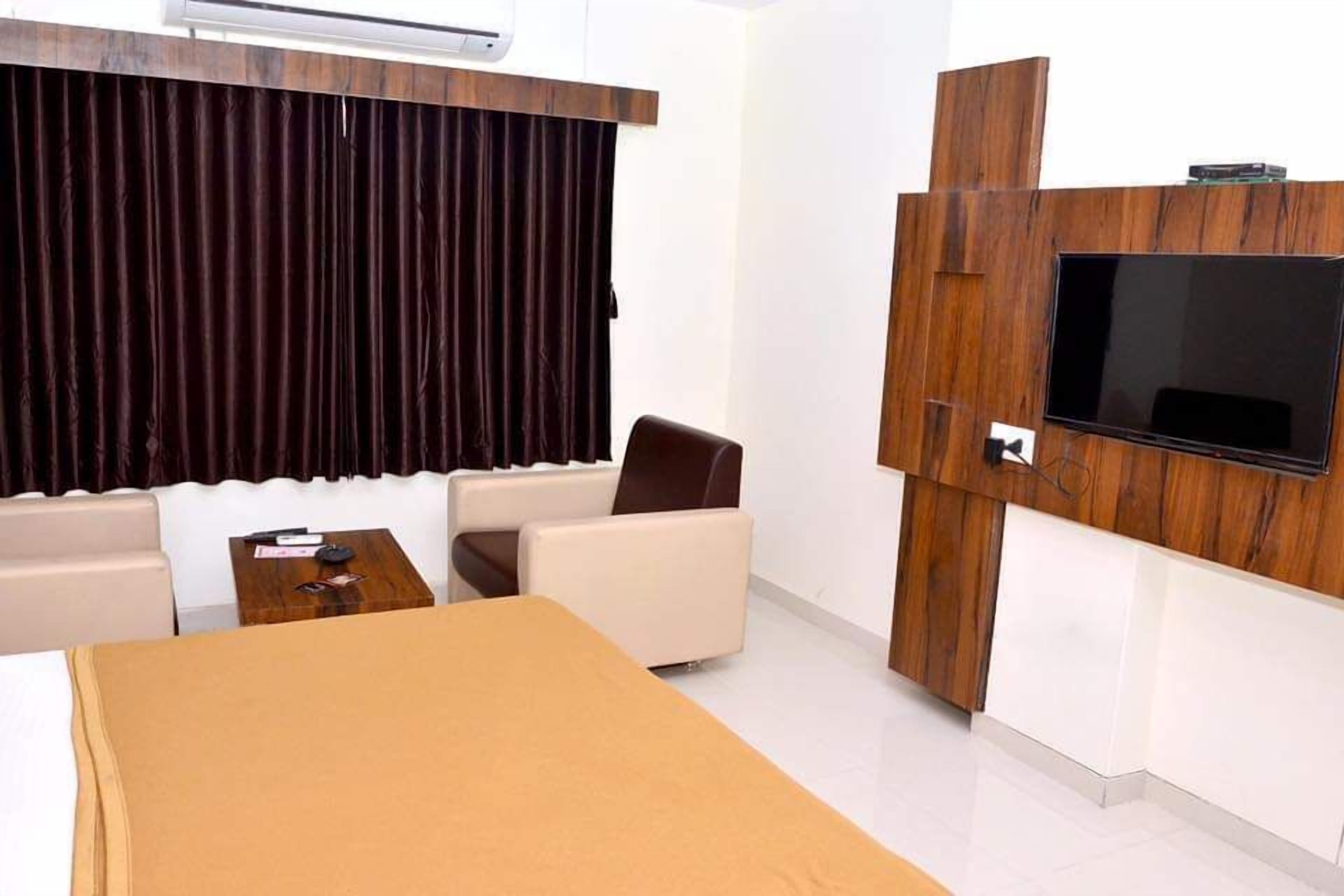 Une chambre d’hôtel moderne dotée d’un téléviseur à écran plat fixé à un mur en bois, d’un canapé, d’une petite table et d’un lit avec une tête de lit en bois.