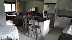 A modern kitchen with a central island, bar stools, a refrigerator, and a dining area with a table and chairs.