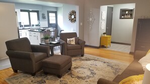 A living room with a brown sofa, a matching ottoman, and a coffee table. There is a decorative wall piece above the sofa.