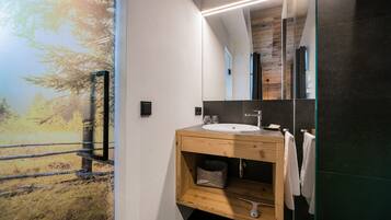 Un baño moderno con tocador de madera, un espejo grande y vista a un bosque a través de una puerta de vidrio.