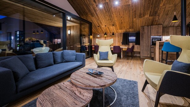 Un intérieur moderne avec un plafond en bois, un canapé, des fauteuils, une table basse ronde et un téléviseur.