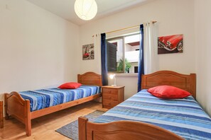 A bedroom with two wooden beds, a nightstand, a mirror, and a window with curtains.