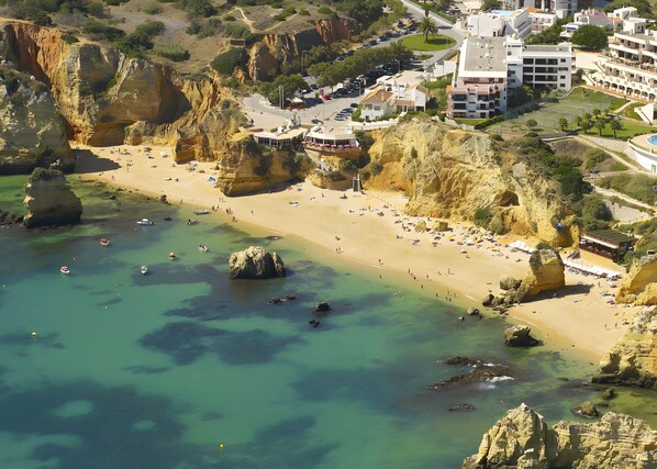 A coastal town with a sandy beach, rocky cliffs, and buildings with balconies overlooking the sea.