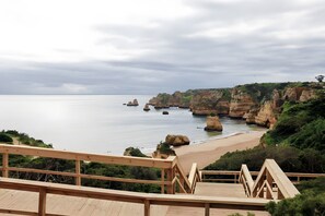 A coastal view with a wooden deck, rocky cliffs, and a beach.