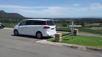 A white minivan parked in a parking lot with a view of a green field and hills in the background.