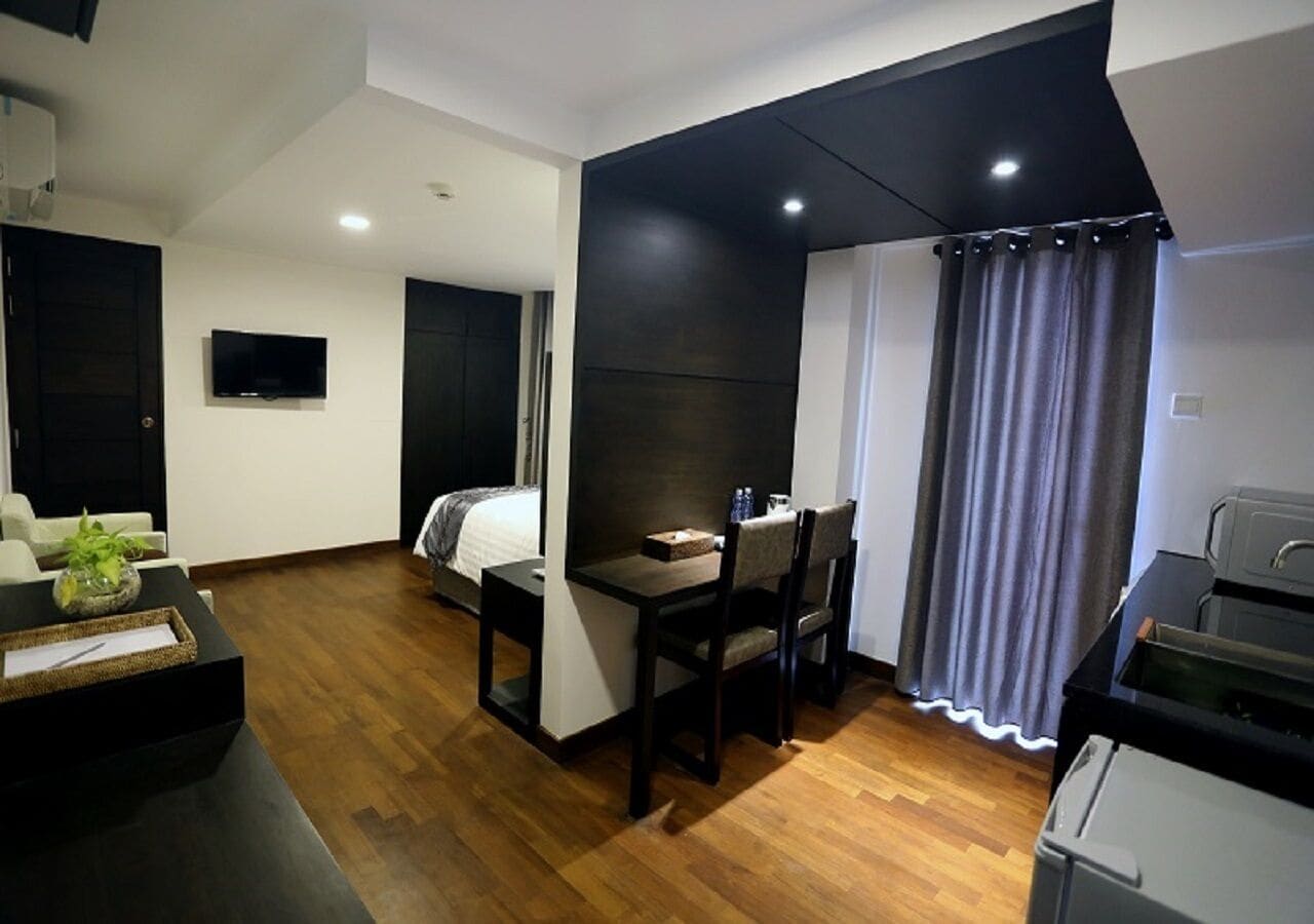 Quarto de hotel compacto com cama, pequena mesa de jantar, televisão e cozinha compacta.