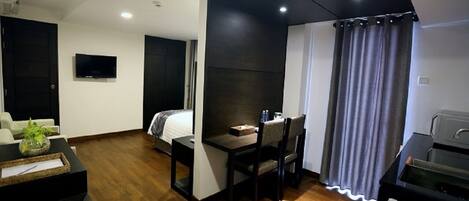 Quarto de hotel compacto com cama, pequena mesa de jantar, televisão e cozinha compacta.