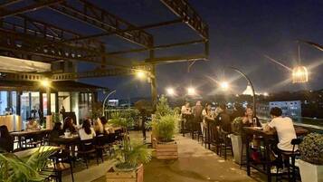 Un área de comedor al aire libre con mesas y sillas, rodeada de plantas en macetas.