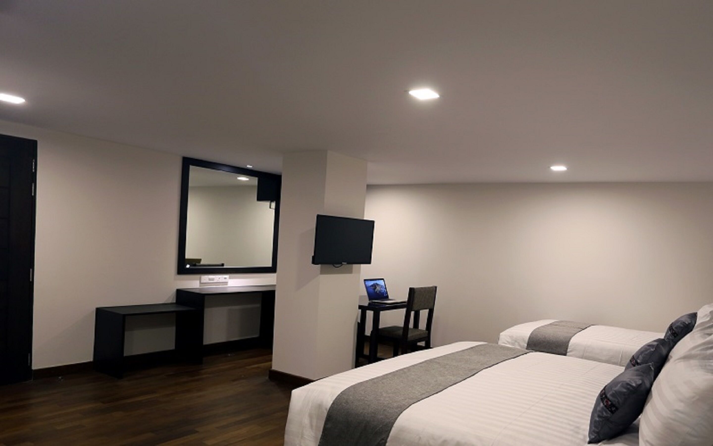 Quarto de hotel com cama, escrivaninha, cadeira, televisão e espelho.