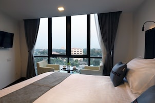 Habitación de hotel con una cama grande, un televisor de pantalla plana montado en la pared, una mesita redonda con dos sillas y vistas a un edificio a través de la ventana.