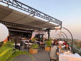 Un espacio exterior para comer con mesas y sillas, rodeado de plantas en macetas y un paseo cubierto.