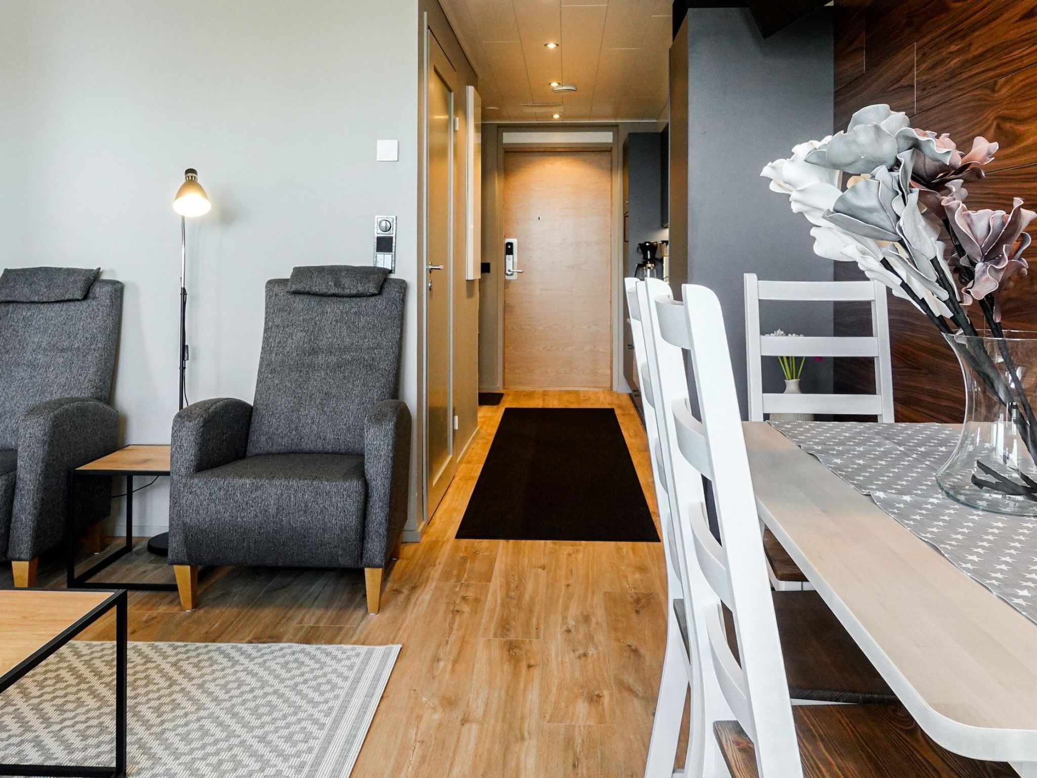 A modern hotel room with two grey armchairs, a wooden dining table, and a white chair.