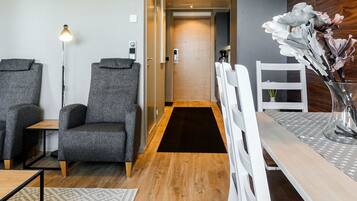 A modern hotel room with two grey armchairs, a wooden dining table, and a white chair.