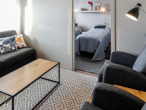 A modern hotel room with a sofa, a small table, a bed with a grey duvet, a mirror, and a wall-mounted lamp. - Levin kunkku b8 by Interhome (Kittilä)