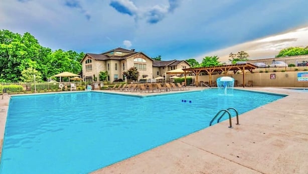 A swimming pool with a fountain, surrounded by a covered patio area and a building with a large window. - Pointe Royale Condo retreat (Branson)