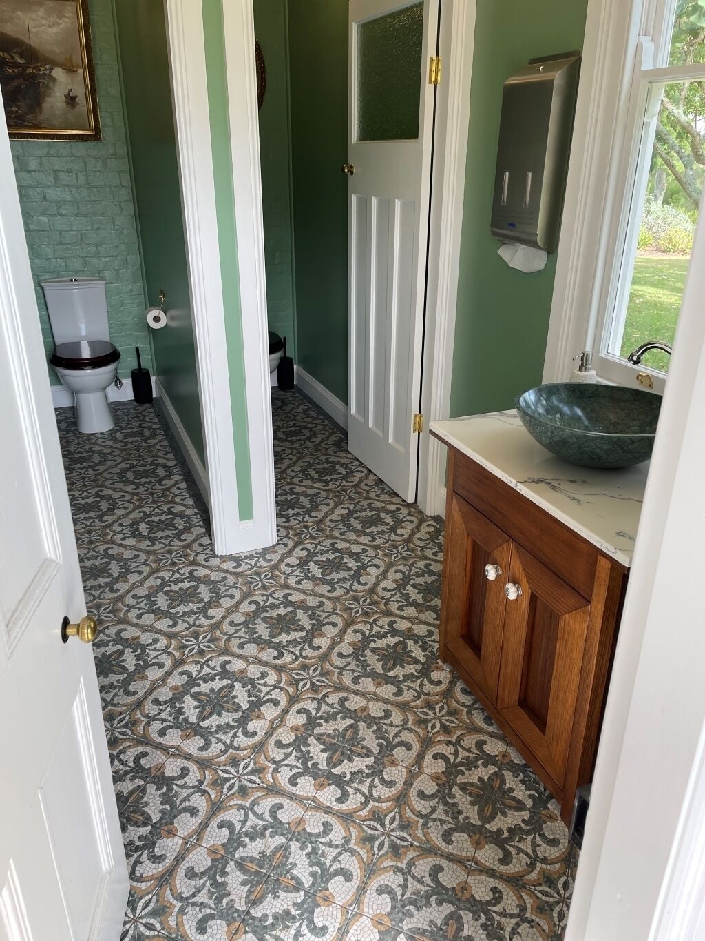 A bathroom with a patterned floor, a toilet, a sink with a mirror, and a door leading to another room.