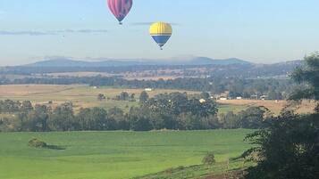 A rural landscape with two hot air balloons in the sky, fields, and distant hills.
