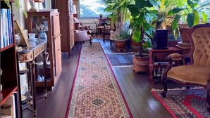 A spacious living room with a long patterned rug, wooden furniture, and various plants.