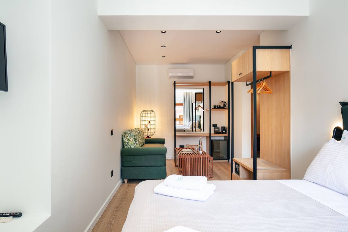 A modern hotel room with a bed, a green sofa, a wooden desk, and a walk-in closet.