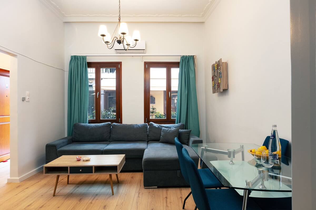 A modern living room with a sectional sofa, a glass dining table, and a chandelier.