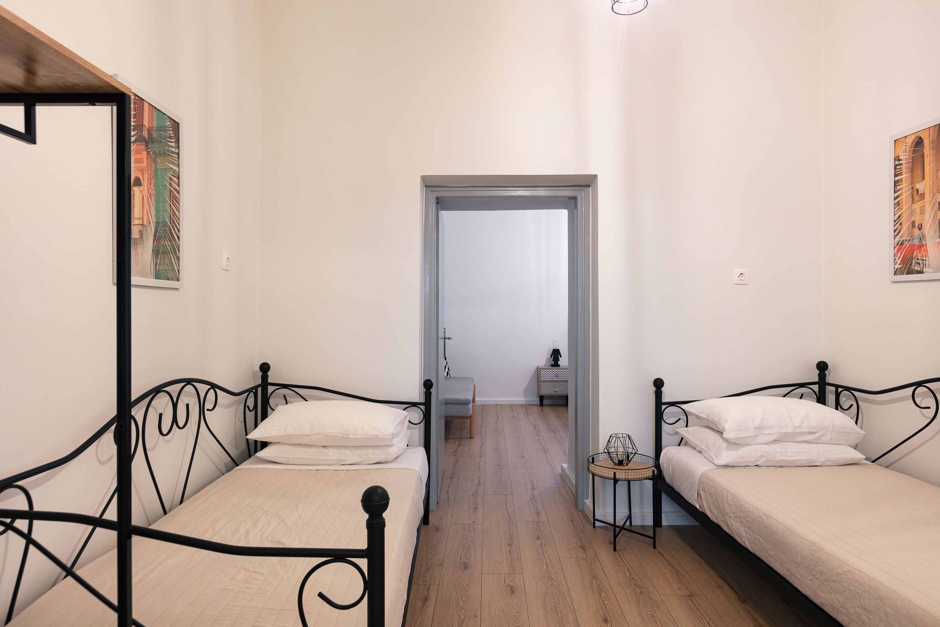 A narrow room with two single beds, a small table, and a chair.