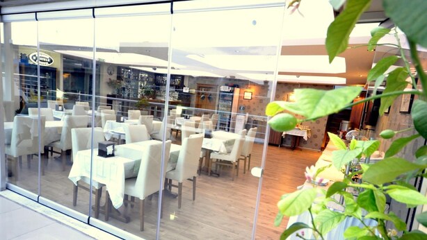 A restaurant with glass walls, white tables, and chairs, and a visible kitchen area in the background. - Khalkedon Hotel Istanbul (Istanbul)