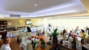 A spacious dining area with multiple tables and chairs, a kitchen area with a buffet setup, and a large window providing natural light. - Khalkedon Hotel Istanbul (Istanbul)