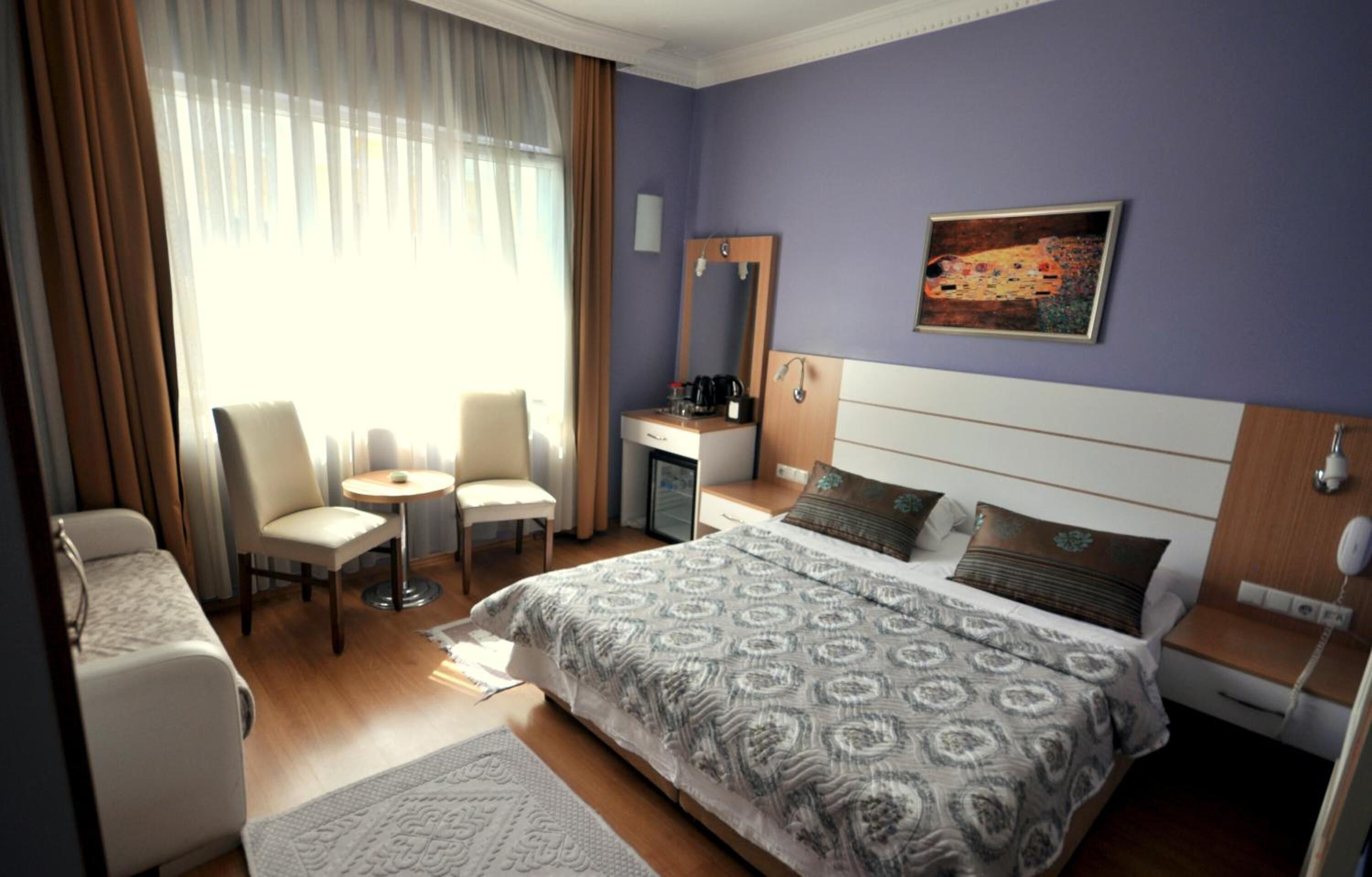 A hotel room with a large bed, a desk, a chair, and a small table.