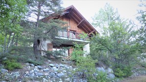 Een chalet met een houten gevel, een balkon, en omgeven door bomen en rotsen.