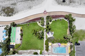 An aerial view of a resort with a swimming pool, lounge areas, and a tennis court.