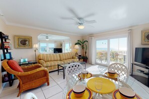 A living room with a sofa, a dining table set with yellow plates, a wicker chair, and a ceiling fan.