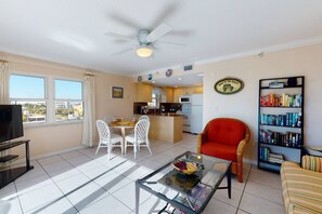 A living room with a glass coffee table, a red armchair, a bookshelf, and a kitchen area with a dining table and chairs.